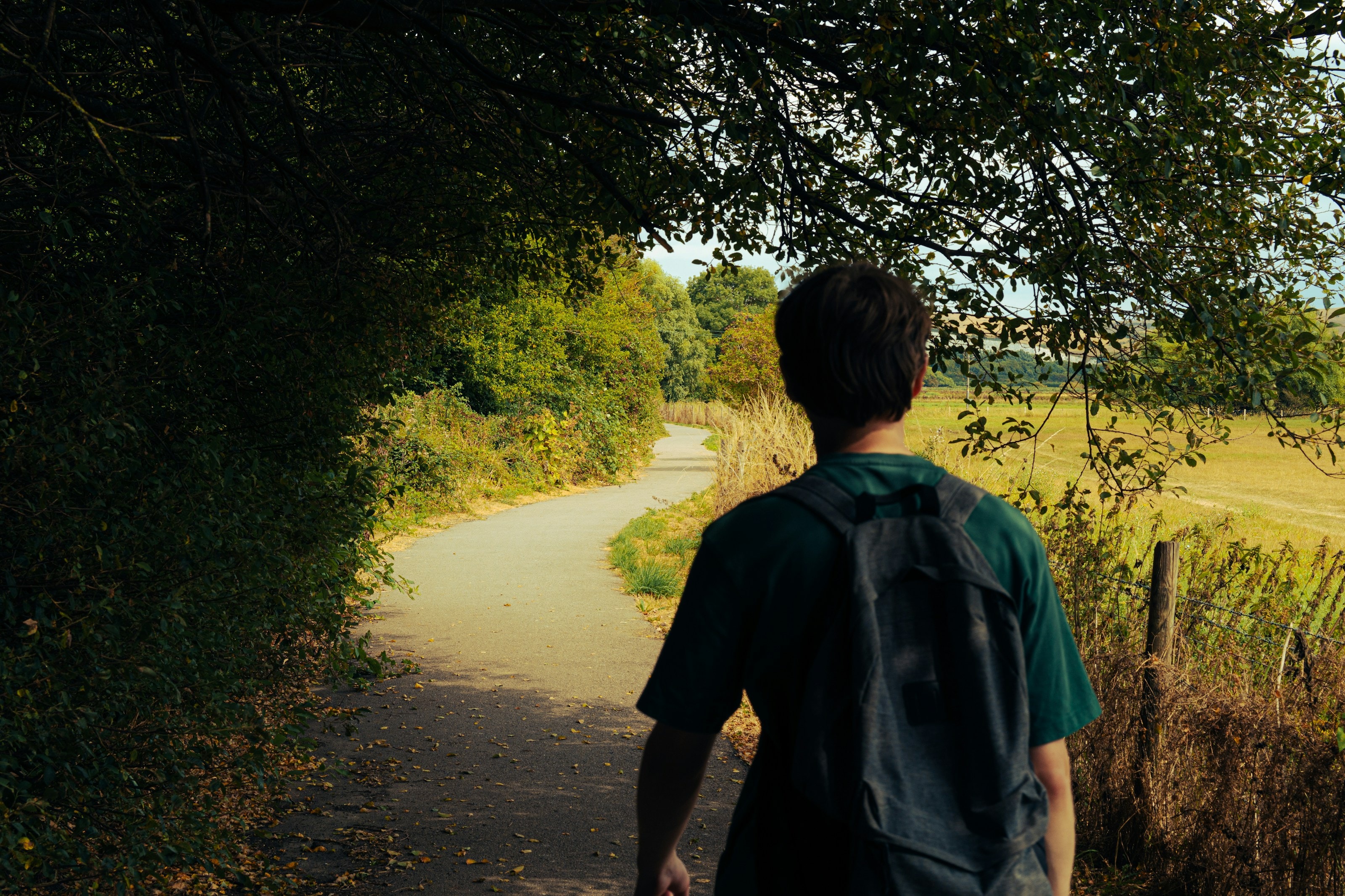 A young person with a backpack walking along a sunlit country path